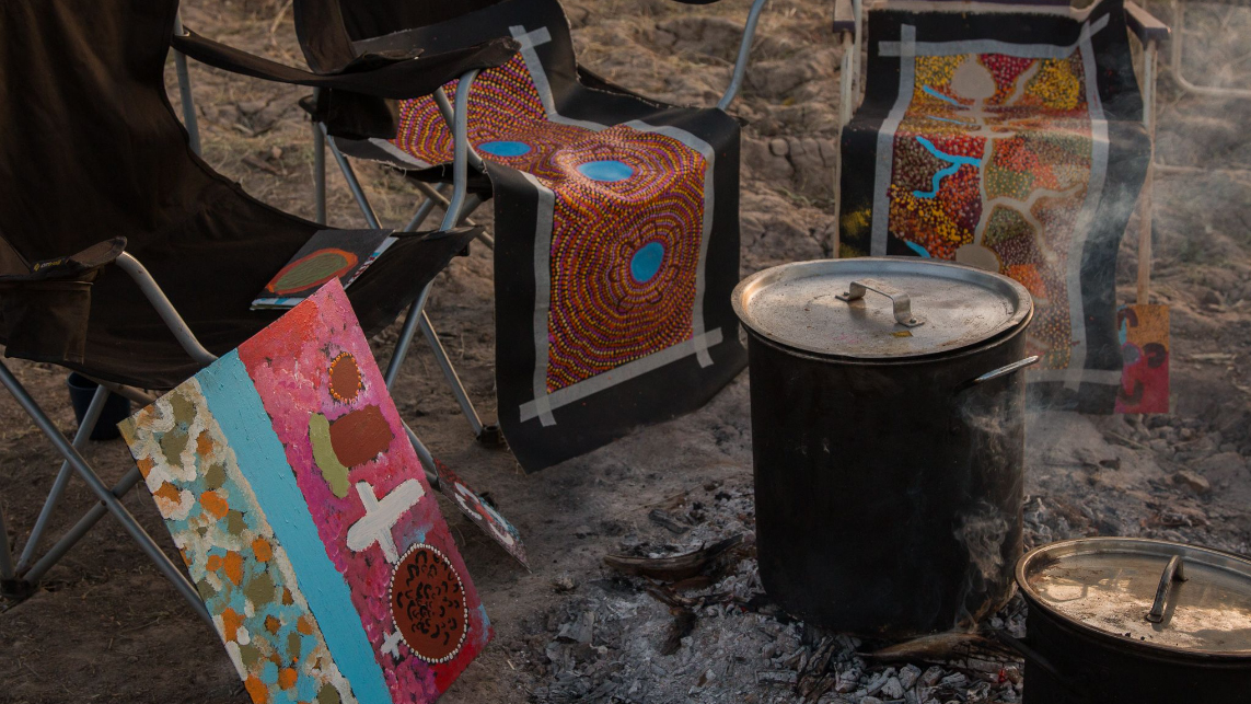 Painting done on Country drying by the fire. Ngurra Kutjuwarra (On Country, Together), Warlayirti Artists Aboriginal Corporation, 2021. Photo by Lucinda White.
