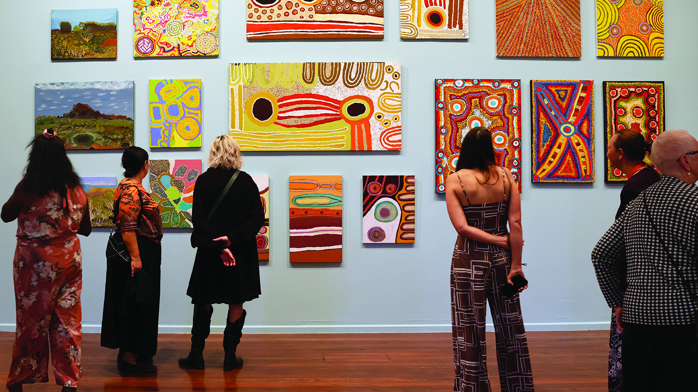 A number of people are viewing an Aboriginal Art works on a gallery wall