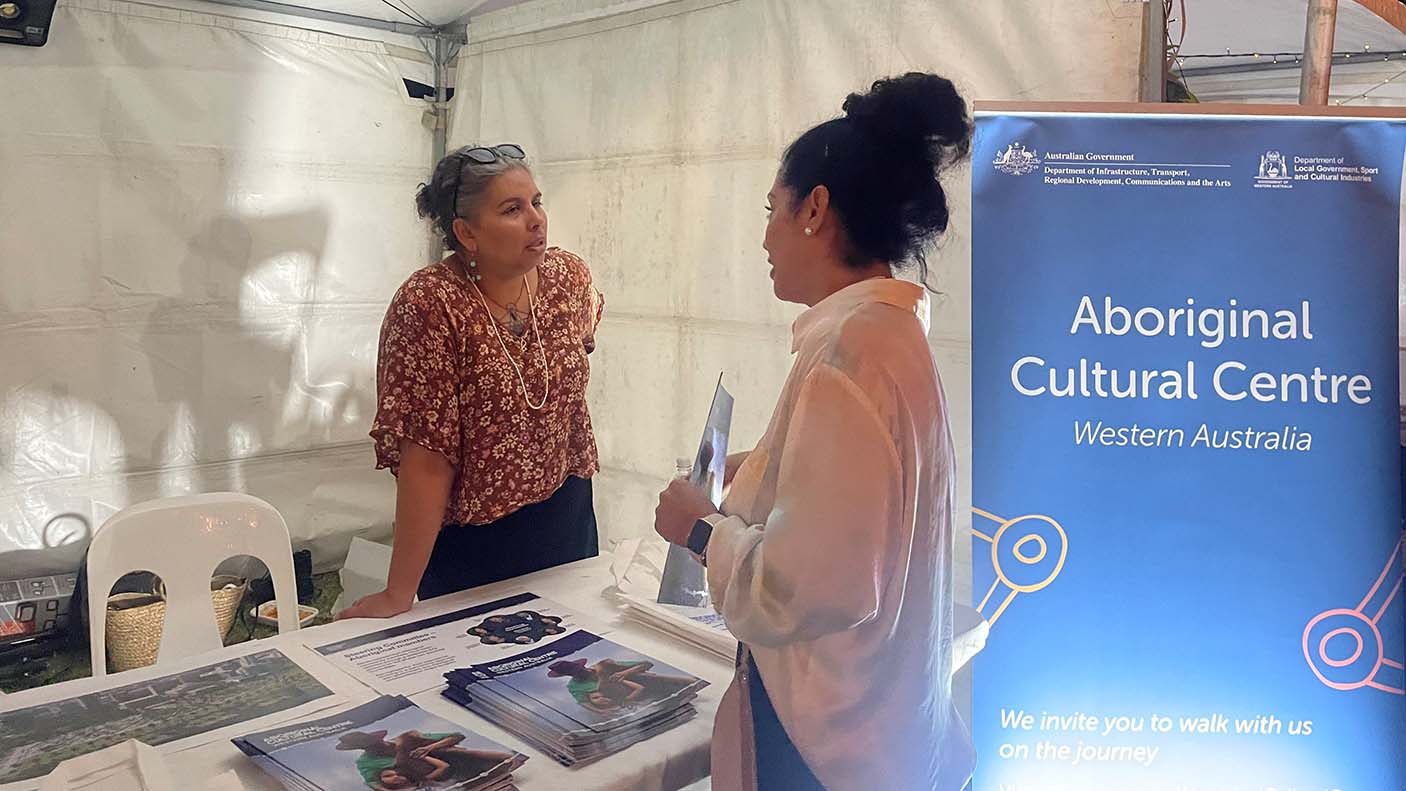 A woman speaking with another woman at a stall with a banner for the Aboriginal Cultural Centre