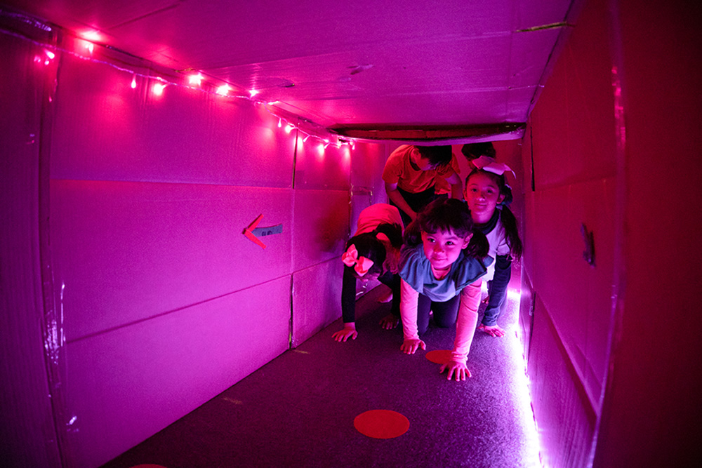 A group of young kids crawling into a cardboard tunnel.