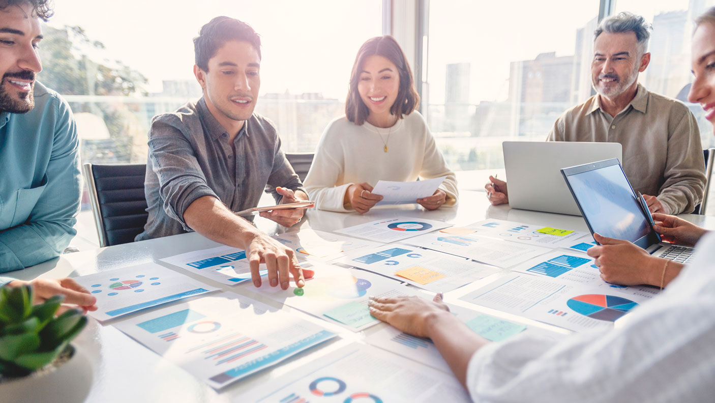 A group sit a meeting table discussing the charts and papers in front of them.