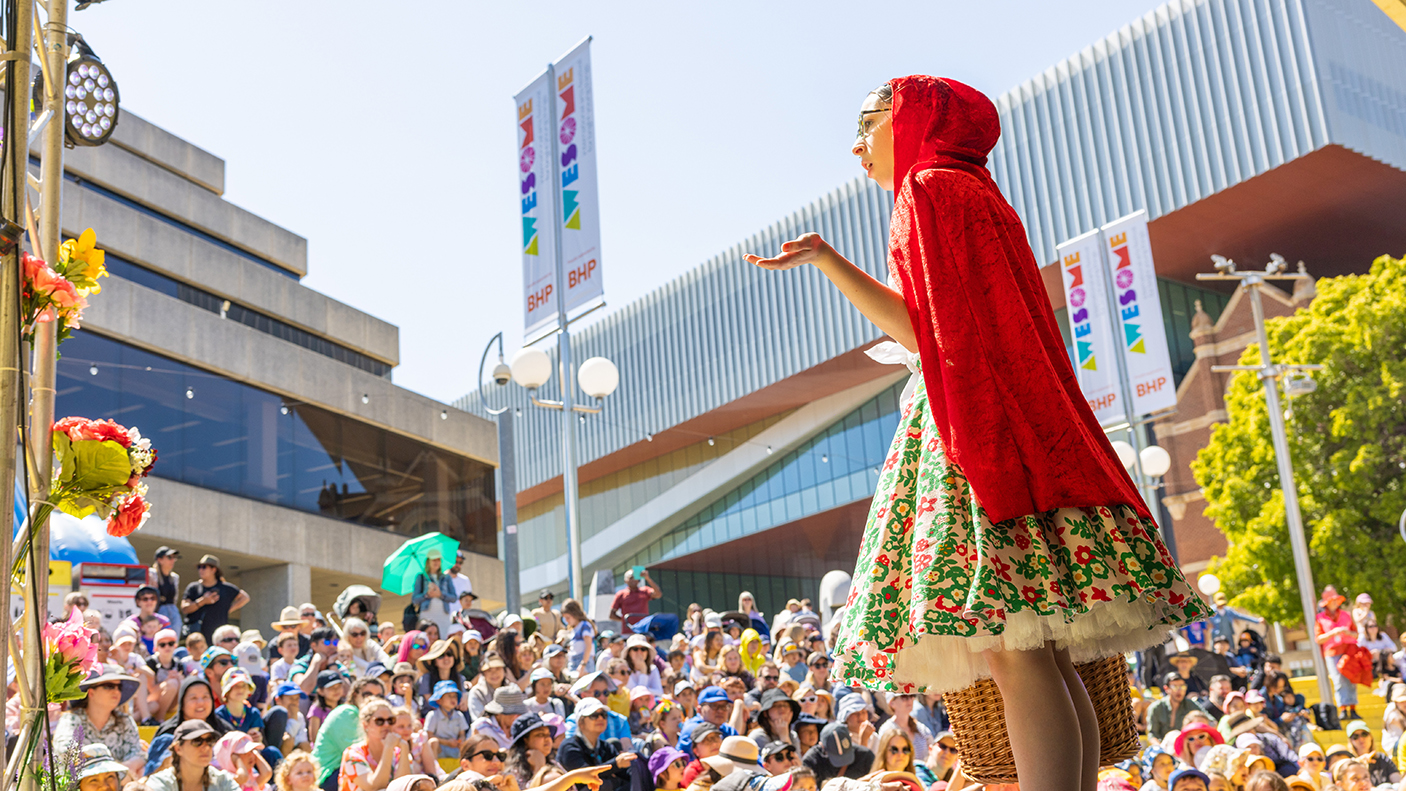 A performer on stage in front of a large crowd of children.