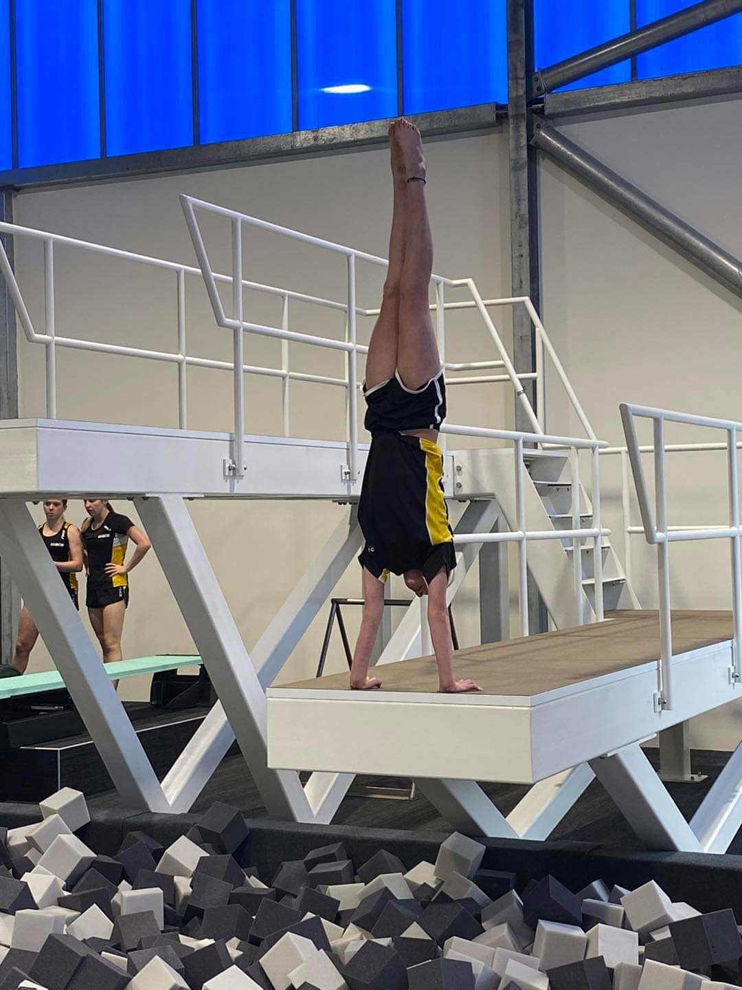 A diver practising their technique, doing an handstand on a platform with a pit of foam blocks below. 
