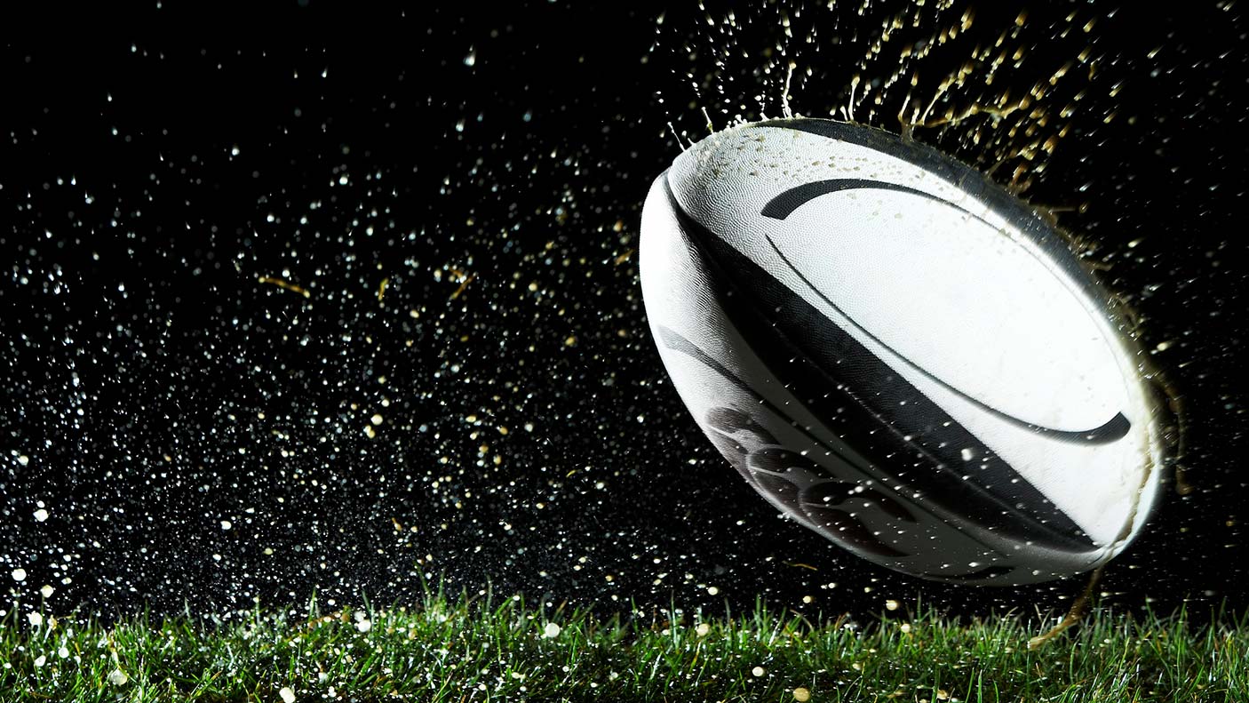 A close-up of a rugby call bouncing on a wet turf with water droplets coming off of the surface.
