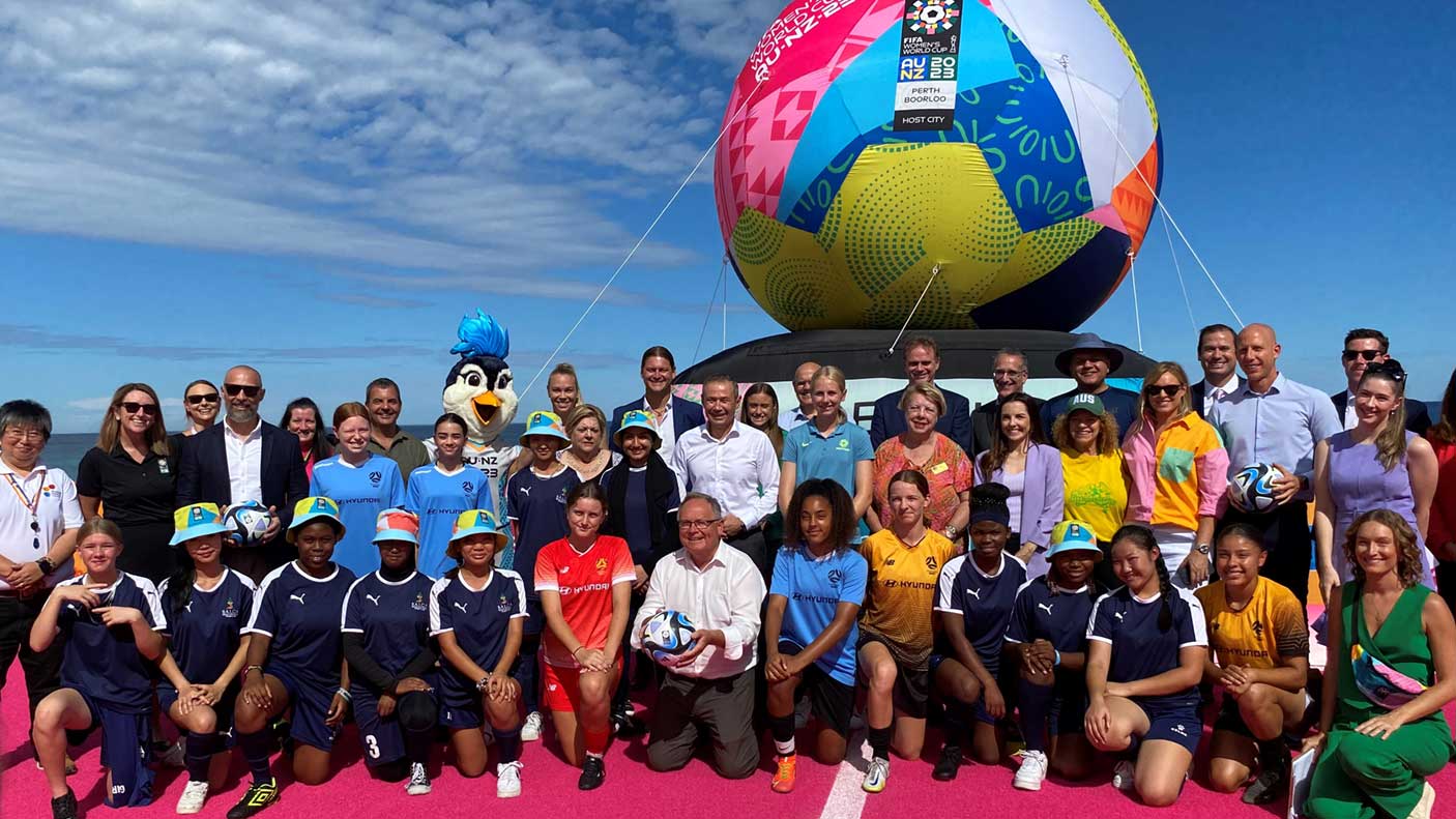 A large group of people standing together in front of a giant colourful ball branded for the FIFA Women's World Cup