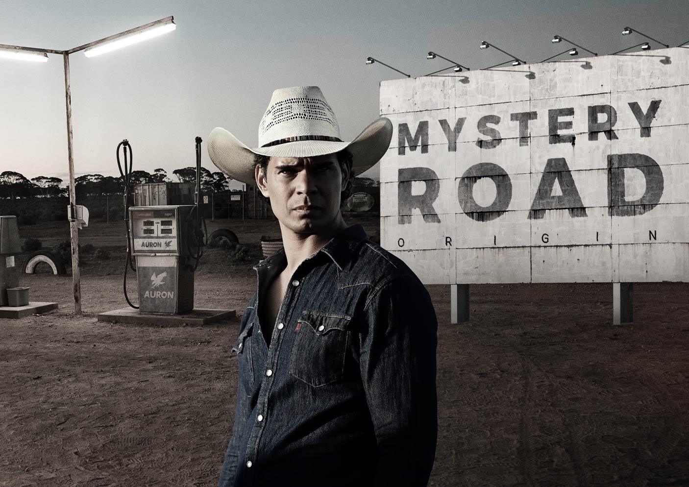 A man wearing a cowboy-style hat in front of a petrol station browser and a billboard reading, 'Mystery Road'