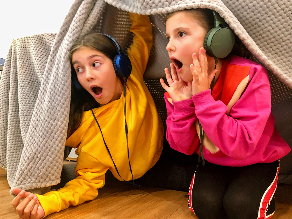 Two girls with headphones looking out of a blanket fort