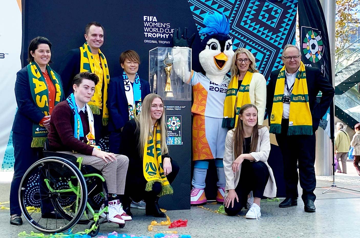 A group of people standing on a stage with Matildas scarves and a mascot