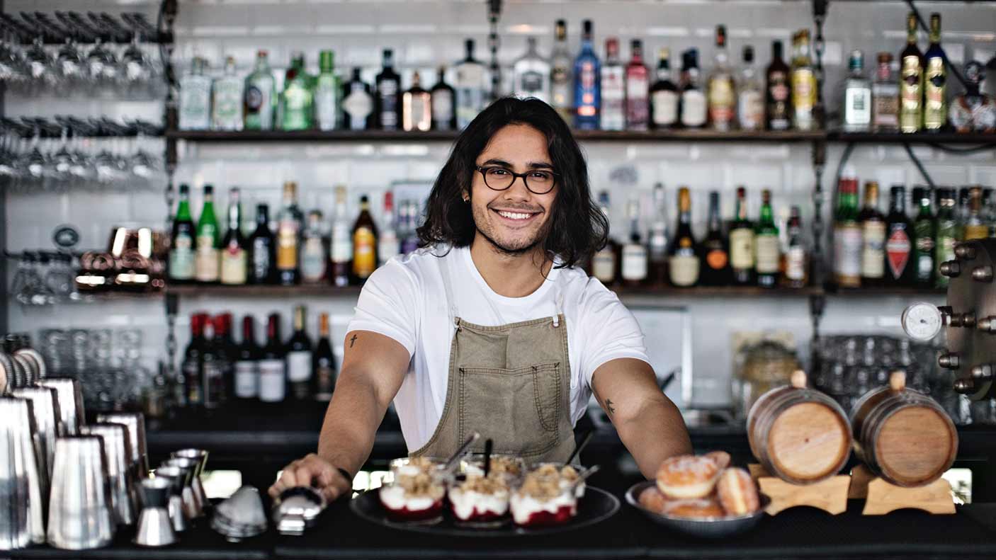 Portrait of smiling owner with food standing at counter in restaurant. Stock photo