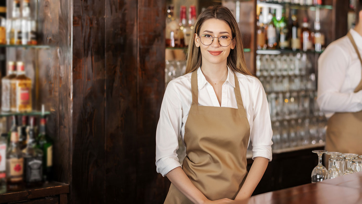 Young work in a hospitality venue stands next to a bar