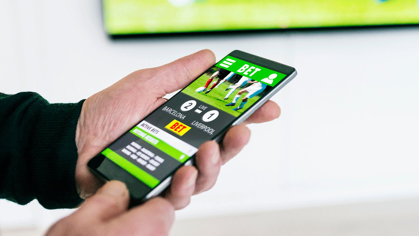 A pair of hands holding a phone with an online betting website on the screen