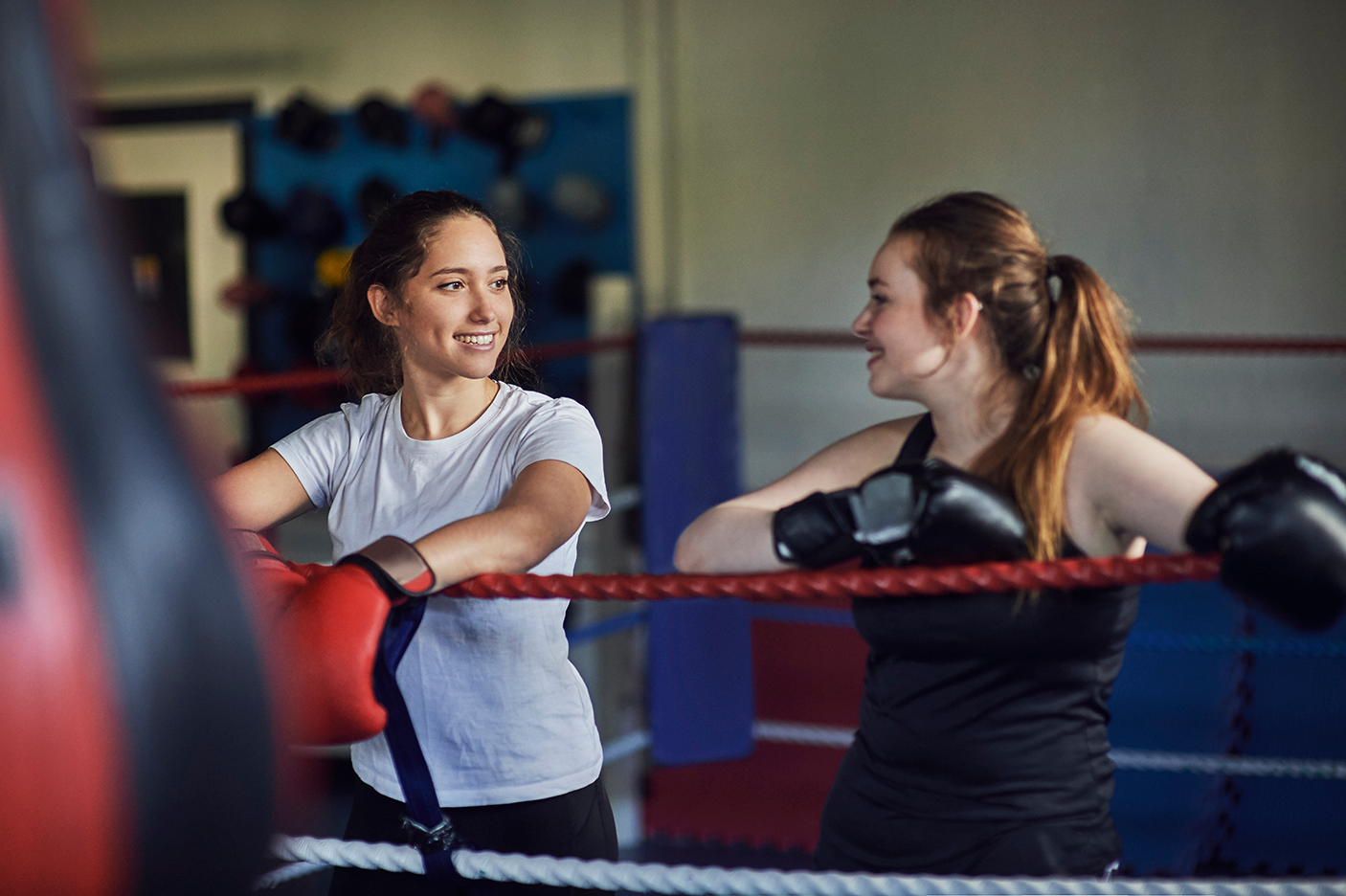 Young female boxers leaning against boxing ring ropes chatting - stock photo