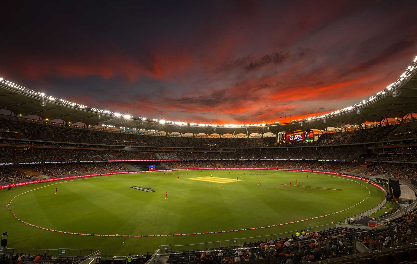 A cricket match in play at Optus Stadium at sunset