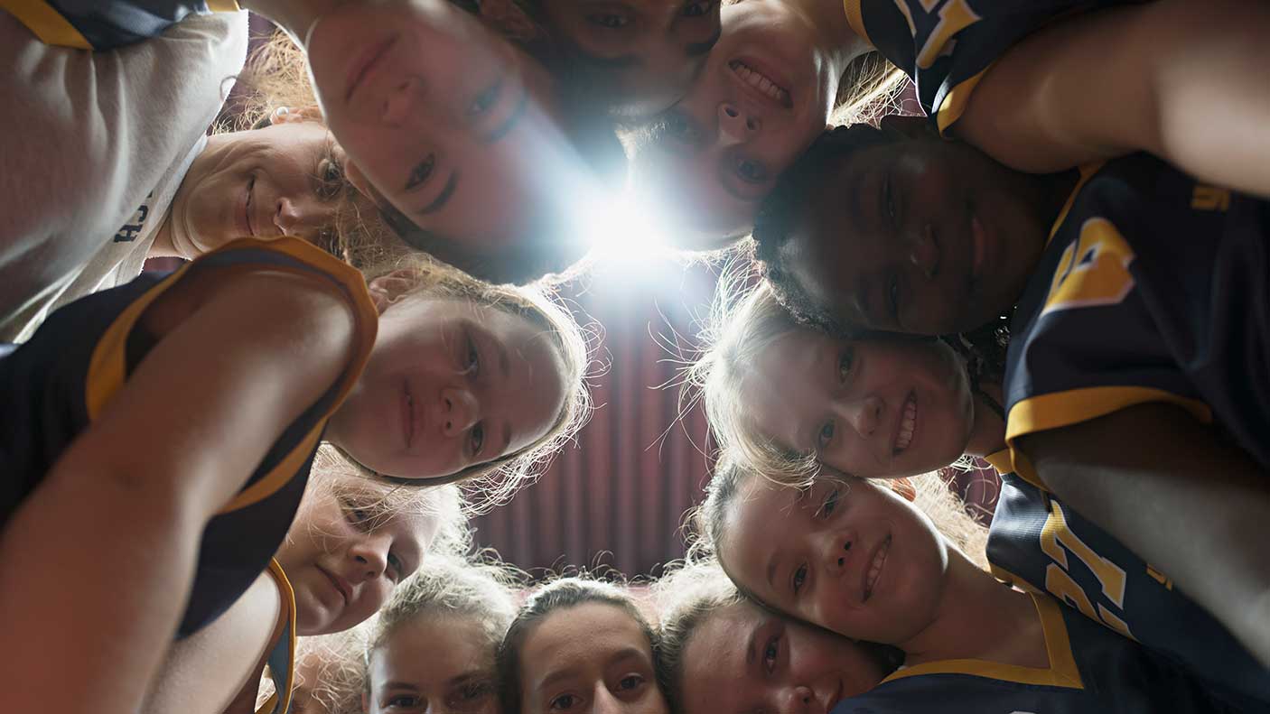 Female basketball players and coach huddling together in circle. Image credit: Joos Mind, Getty Images