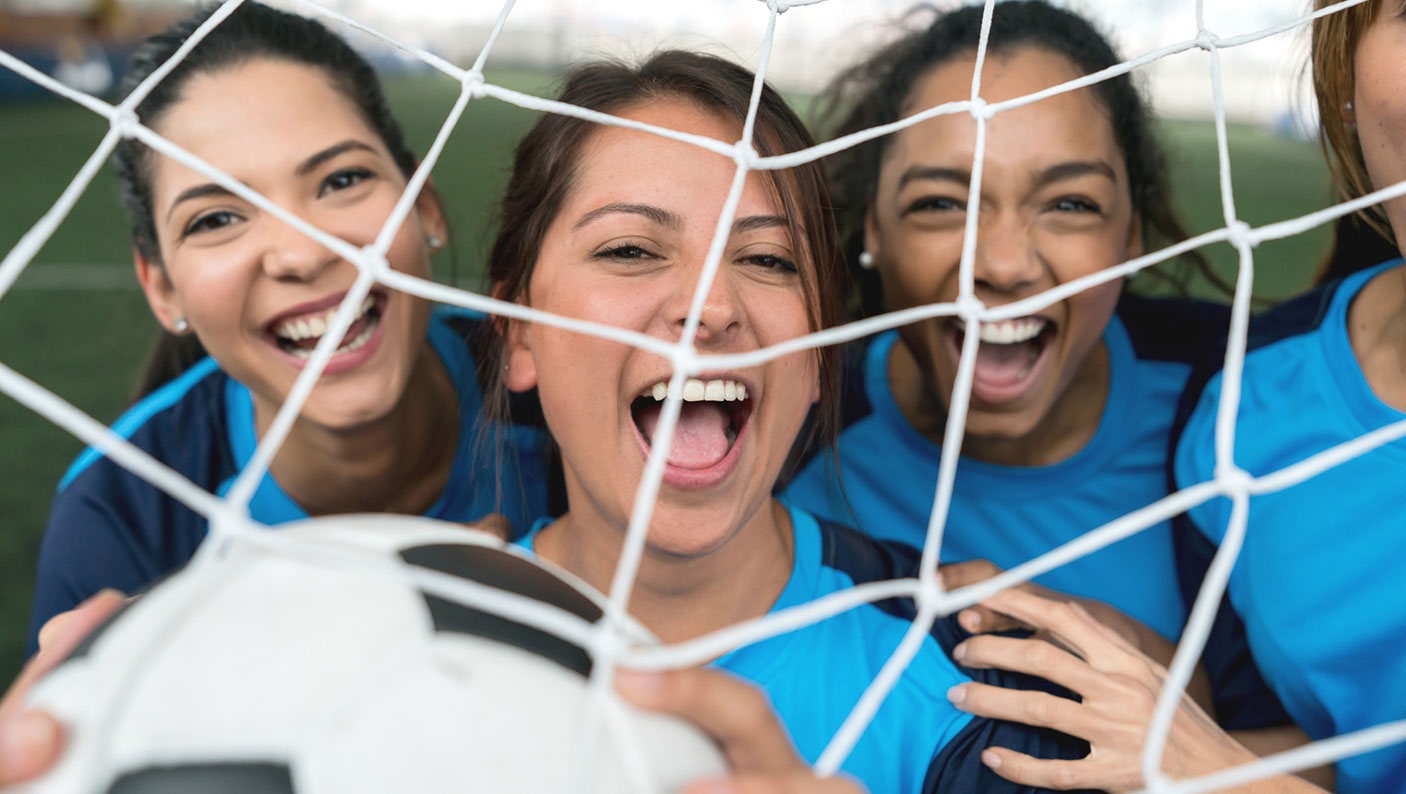 4 women football players hold a football behind the goal nets